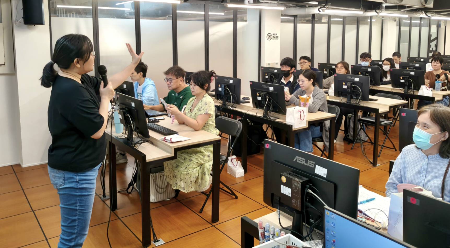 林思翰在高師大 AI 短影音工作坊持麥克風授課,學員在電腦教室參與課程